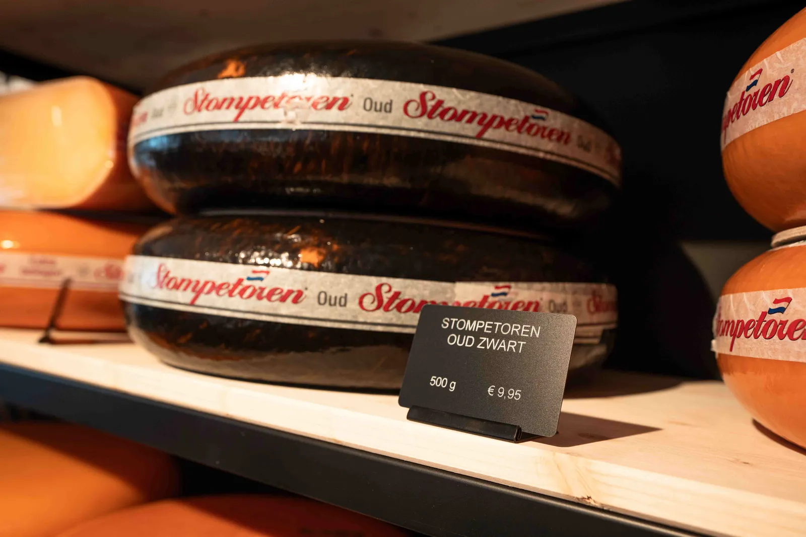 Stompetoren Oud Zwart kaaswielen met prijskaartje op houten schap