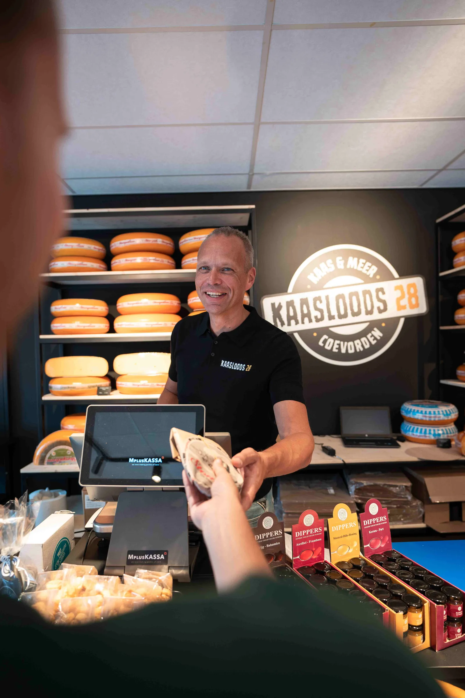 Verkoper overhandigt lachend een stuk kaas aan een klant